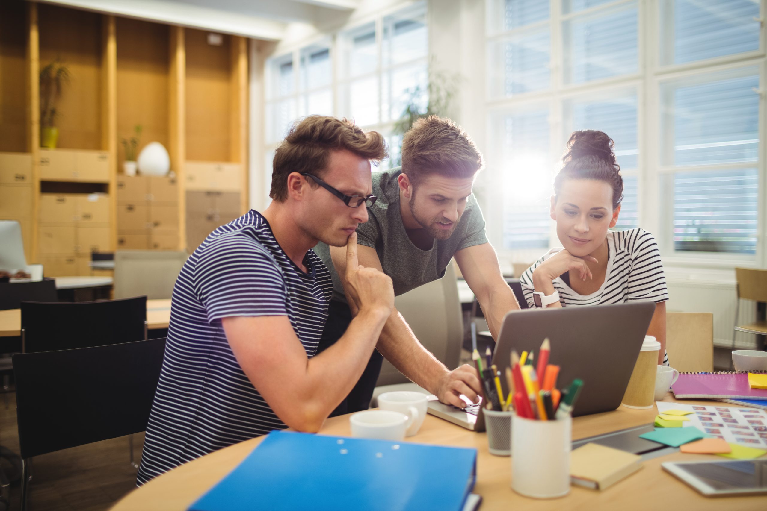 Group of graphic designers discussing over laptop at their desk Gambar Ditekindo